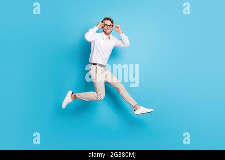 Vue sur toute la longueur de la taille du corps attrayant amusant homme jumpant courir touchant les spécifications isolées sur fond bleu clair de couleur Banque D'Images