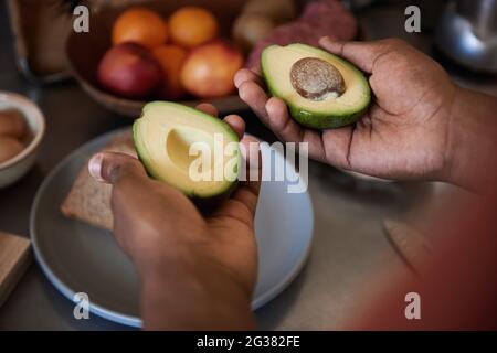 Homme africain tenant deux moitiés d'un avocat dans sa cuisine Banque D'Images