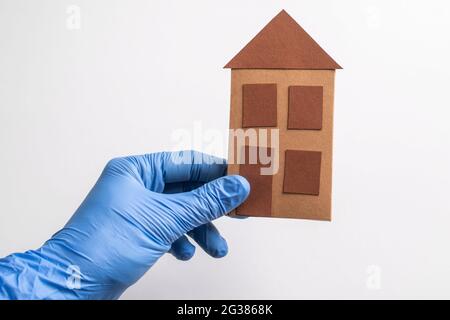 Main dans un gant tenant une maison en papier sur fond blanc Banque D'Images
