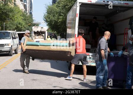 Austin, Texas, États-Unis. 14 juin 2021. Les employés de la ville transportent un grand canapé alors qu'ils nettoient un grand camp de protestation pour sans-abri sur le côté nord de l'hôtel de ville du centre-ville. La police a arrêté plusieurs sans-abri qui ont refusé de coopérer après plusieurs semaines d'avertissements et d'offres d'assistance. Crédit : Bob Daemmrich/Alamy Live News Banque D'Images