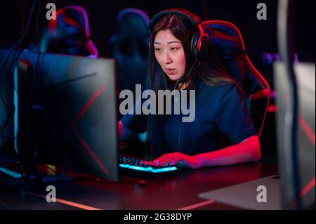 Une jeune fille asiatique joue à des jeux vidéo en ligne le soir dans un club informatique. Banque D'Images