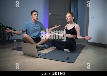 La maison des jeunes mariés pour les cours de yoga, ils méditent sur le sol sous une vidéo avec de la musique relaxante à partir d'un ordinateur portable. Banque D'Images