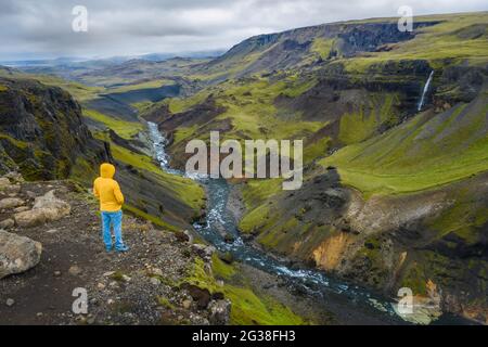 Vue aérienne de l'homme appréciant le paysage islandais de la vallée des hautes terres et de la rivière Fossa avec ruisseau bleu et collines vertes et falaises couvertes de mousse. Banque D'Images