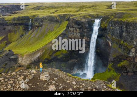 Vue aérienne de l'homme se tenant sur le bord de la falaise en profitant de la vallée des montagnes de l'Islande et de la cascade de Haifoss Banque D'Images