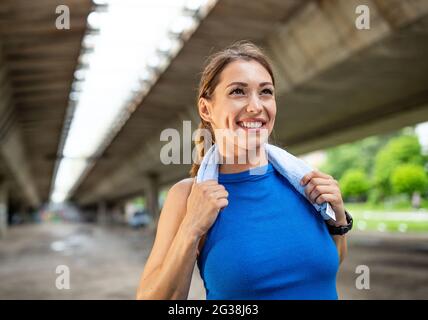 Jeune femme sportive se détendant après l'entraînement à l'extérieur sous le pont. Posez une serviette anti-transpiration sur le cou. Banque D'Images