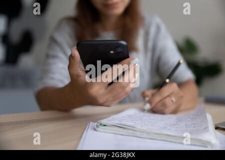 Femme en gros plan tenant le téléphone, prenant des notes, écrivant des informations importantes Banque D'Images