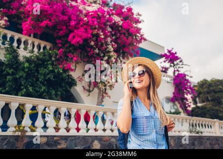 Une femme touristique parle au téléphone dans la rue avec des fleurs de bougainvilliers. Bonne femme portant un chapeau et un sac à dos. Voyage d'été Banque D'Images