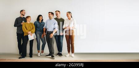Un groupe de professionnels qui se tiennent contre un mur blanc. Les créatifs d'affaires heureux rient les uns avec les autres. Banque D'Images