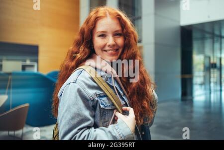 Belle fille regardant l'appareil photo et souriant en se tenant à l'université. Jeune femme qui va en classe à l'école secondaire. Banque D'Images