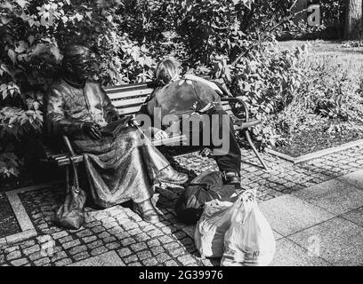 Varsovie, Mazowieckie, Pologne, 27 juin 2020, homme sans abri dormant sur le banc à côté du monument du Père Jan Twardowski Banque D'Images