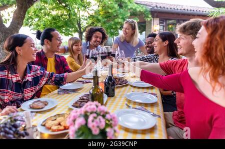 grand groupe de personnes multiéthiques qui apprécient le dîner-barbecue en plein air assis sur une table de jardin pour manger et toaster le vin. grand ami heureux varié Banque D'Images