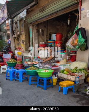 Un marchand de fruits et légumes de rue lisant un journal à l'extérieur de son magasin à Hanoi, Vietnam Banque D'Images