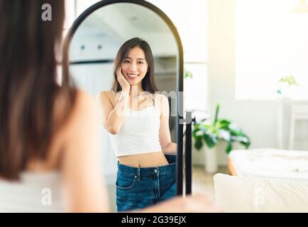 jeune femme portant de grands jeans avant de perdre du poids, regardant la figure devant le miroir, est très heureuse qu'elle ait perdu du poids réussi Banque D'Images