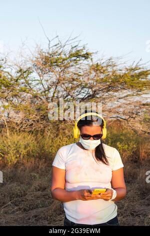 Femme avec masque de protection écoutant de la musique avec un téléphone cellulaire et un casque dans le champ Banque D'Images
