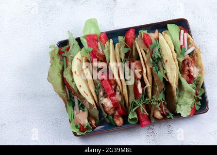 Tacos avec salade verte, poivre, poulet sur une assiette carrée sur fond gris clair. Vue de dessus, plan d'appartement Banque D'Images