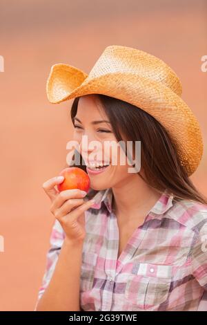 USA cowgirl mangeant pêche nectarine fruit sourire portant chapeau de cowboy à la ferme extérieure de campagne . Les agriculteurs de nourriture saine marché avec beau jeune mélange Banque D'Images