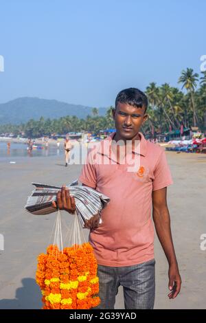 Jeune saleman de journal indien posant avec des guirlandes de fleurs sur Palolem Beach, Goa, Inde Banque D'Images