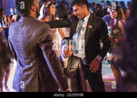 Un jeune garçon indien portant des costumes de mariage danse entre deux invités de mariage masculins indiens sur le dancefloor, Palolem, Goa, Inde Banque D'Images