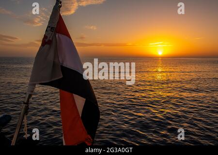 Drapeau de l'Égypte agitant sur un navire avec beau coucher de soleil orange et violet sur la mer Rouge en arrière-plan. Banque D'Images