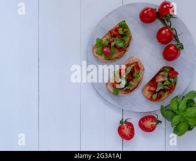 Trois bruschetta aux tomates et basilic frais sur un panneau en bois blanc Banque D'Images