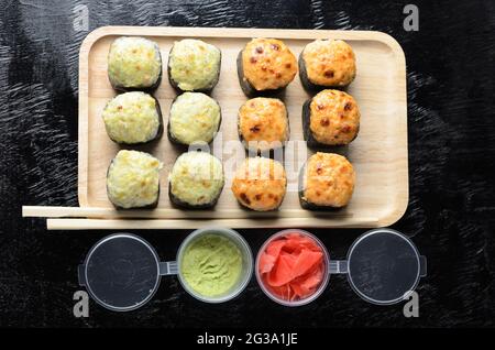 Un ensemble de rouleaux de riz aux fruits de mer enveloppés de fines feuilles d'herbe de mer séchées sur un plateau en bois avec du gingembre et du wasabi sur un fond en bois noir. Sélectif Banque D'Images