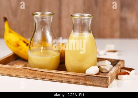 Deux bocaux à boire avec smoothies à la banane jaune et à la noix de coco sur un comprimé en bois Banque D'Images