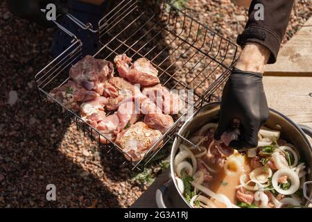 Cuisson du shashlik sur un gril, le cuisinier dépose des cubes de dinde dans une grille métallique Banque D'Images