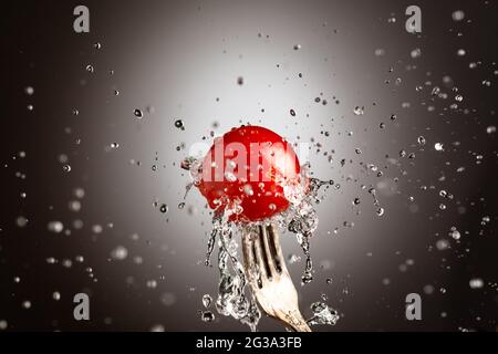 Tomates cerises mûres dans des éclaboussures d'eau sur une fourchette Banque D'Images