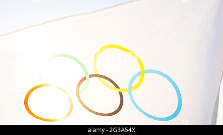 Le drapeau olympique flotte dans le vent contre le fond du ciel et le soleil en gros plan. Le symbole des Jeux Olympiques de Sports, fans de come Banque D'Images