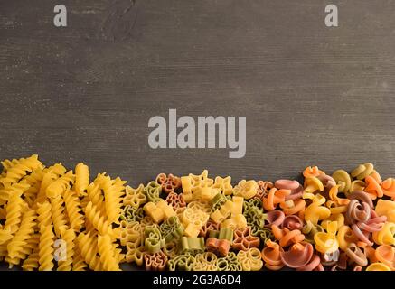 Pâtes crues de différentes couleurs et de différents types disposées sur une table en bois foncé en dessous de la photo Banque D'Images