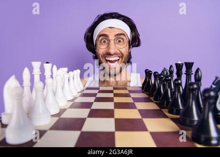 Photo de gai positif fou jeune homme émerveillé visage porter lunettes joueur d'échecs isolé sur fond violet de couleur Banque D'Images