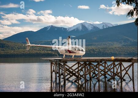 Scène tranquille, hélicoptère sur une plate-forme d'atterrissage au-dessus d'un lac clair et calme avec un magnifique fond de montagne enneigé Banque D'Images