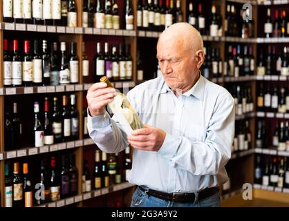 Le retraité confiant choisit le vin blanc dans un magasin de spiritueux Banque D'Images