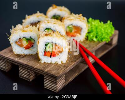 Katsuobushi Uramaki Sushi Roll avec saumon et concombre sur panneau en bois sur fond noir. Roulé à sushis avec flocons de bonito de poisson secs Banque D'Images