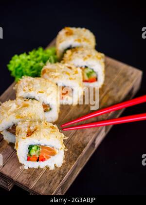 Katsuobushi Uramaki Sushi Roll avec saumon et concombre sur panneau en bois sur fond noir. Roulé à sushis avec flocons de bonito de poisson secs Banque D'Images