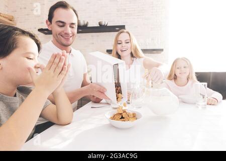 Les enfants et les parents prennent le petit-déjeuner. Famille mangeant des céréales avec du lait Banque D'Images