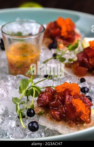 Fermer le tartare de thon rouge dans la glace sur la plaque verte avec de la chaux et des bleuets. Arrière-plan marron en bois Banque D'Images