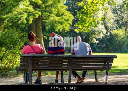 Trois personnes assises sur un banc dans un parc Vondelpark d'Amsterdam ensoleillé et verdoyant aux pays-Bas. Banque D'Images