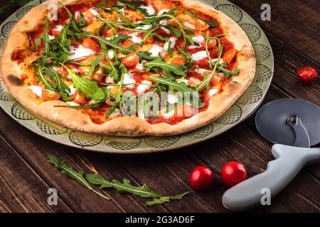 Gros plan Pizza Margherita avec mozzarella de Buffalo, tomates et basilic frais. Le coupe-pizza repose sur un fond en bois. Restauration rapide italienne traditionnelle Banque D'Images