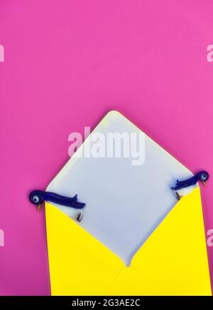 Deux figurines de pingouin en verre mignonnes sur les côtés de l'enveloppe jaune sur fond rose. Concept de contemplation, évasion, Banque D'Images