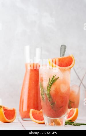 Smoothie au pamplemousse rafraîchissant au froid, au romarin et à la glace en verre, quartiers de pamplemousse et branches de romarin sur la table, fête à la maison Banque D'Images