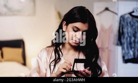 jeune femme en soie rose peignoir tenant des ombres à paupières et une brosse cosmétique dans la chambre Banque D'Images