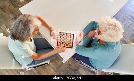 Deux femmes âgées à la retraite jouant aux dames comme activité de loisirs à la maison Banque D'Images