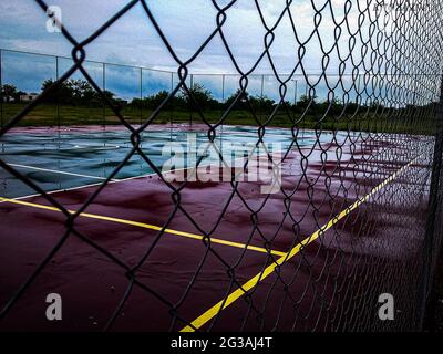 Netball ou basket-ball humide emptycourt lors d'une sombre journée de pluie de derrière la clôture en maille de fil Banque D'Images