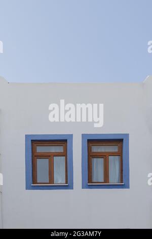 Un bâtiment blanc avec des cadres de fenêtre bleus contre un ciel bleu dans le style grec. Concept de voyage et d'architecture Banque D'Images