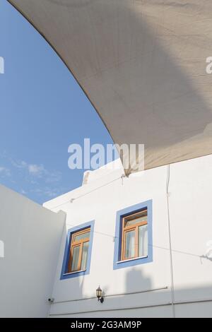 Un bâtiment blanc avec des cadres de fenêtre bleus contre un ciel bleu dans le style grec. Concept de voyage et d'architecture Banque D'Images