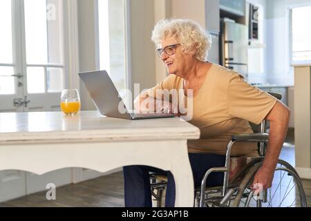 Une femme âgée en fauteuil roulant passe un appel vidéo sur un ordinateur portable avec sa famille à la maison Banque D'Images