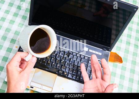 Carnet avec un café versé dans une tasse. Accident informatique. Ordinateur portable détruit avec du liquide. Café renversé sur le clavier de l'ordinateur portable. Renverser du café Banque D'Images