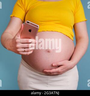 Une femme enceinte regarde l'écran de l'iPhone sur fond bleu - Moscou, Russie, 23 avril 2021 Banque D'Images