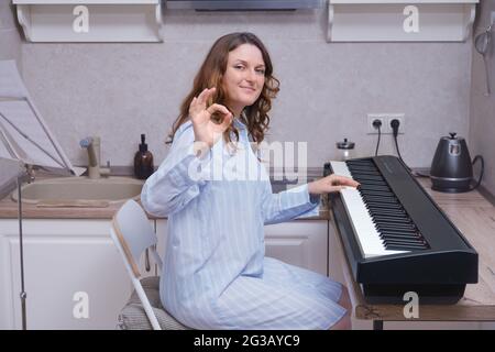 Une musicienne dans une queue bleue s'assoit au piano et fait un geste de main OK en accord Banque D'Images